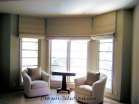 Fused fabric blacked-out roman shade by a bay window by Drapery Solutions.